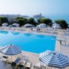 Piscina all'aperto con ombrelloni blu e bianchi, vista mare e un castello in lontananza.