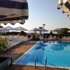 Piscina con sedie a sdraio sotto ombrelloni a righe blu e bianche, e un cielo limpido.