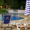 Piscina illuminata di notte, circondata da sedie a sdraio e ombrelloni a righe bianche e blu.