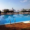 Piscina rettangolare con lettini e ombrelloni a righe bianche e blu. Cielo sereno sopra.