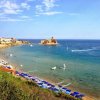Spiaggia affollata con ombrelloni blu, castello in lontananza.