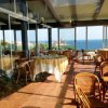 Ristorante con grandi vetrate vista mare, tavoli apparecchiati e sedie in rattan.