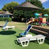 Lettini da sole sotto ombrelloni e un'area giochi con scivoli colorati su prato verde.