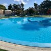 Piscina circolare all'aperto con recinzione blu e giochi per bambini sullo sfondo.
