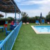 Piscina con sdraio colorate e area giochi coperta da tettoia di legno.