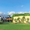 Edifici bianchi e gialli immersi nel verde con cielo blu e alcune nuvole.