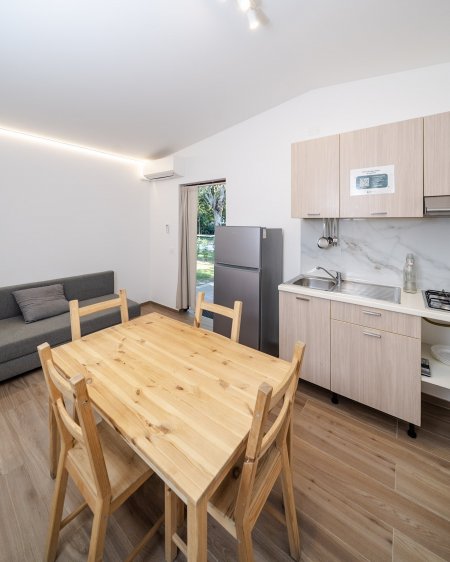 Soggiorno moderno con tavolo in legno e cucina attrezzata.
