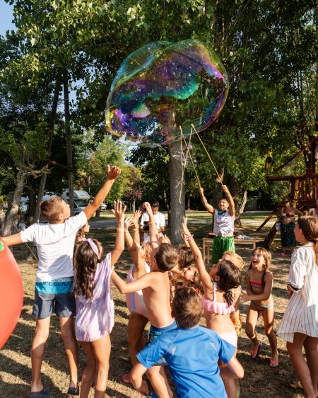 Bambini giocano con una bolla gigante in un parco.