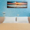 Una camera d'albergo con letto matrimoniale e parete blu decorata. Quadro di un tramonto sul mare.