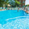 Piscina all'aperto con persone nuotanti e sdraiate nei lettini sotto ombrelloni.