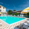 Piscina circondata da lettini bianchi e ombrelloni giallo-bianco. Edificio chiaro sullo sfondo.
