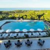 Vista di una piscina con ombrelloni, circondata da verde e vista mare.