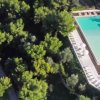 Piscina rettangolare tra alberi e area relax.