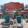 Ombrelloni a righe rosse e verdi con lettini verdi su una spiaggia sabbiosa.
