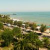 Vista dall'alto di una spiaggia con ombrelloni, strada e auto parcheggiate.