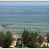 Mare calmo con persone sulla battigia e ombrelloni su una spiaggia alberata.