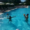 Persone giocano a pallanuoto in piscina sotto ombrelloni.