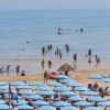 Spiaggia affollata con bagnanti e ombrelloni colorati.