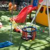 Area giochi con altalene, scivolo e giochi su erba sintetica.