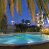 Piscina illuminata di sera, palme e hotel sullo sfondo.