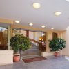 Ingresso di un hotel con due grandi piante in vaso e tappeto marrone.