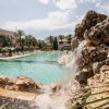 Cascata rocciosa e piscina con palme.