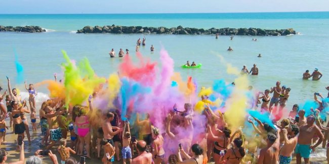 Persone lanciano polveri colorate su una spiaggia.