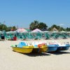Spiaggia con pedalò colorati e lettini sotto ombrelloni colorati.