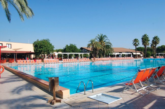 Piscina con lettini arancioni e palme.
