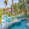Un giardino con alberi tropicali e piscine attraversate da ponticelli blu.
