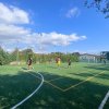 Giocatori su un campo da calcio illuminato, recintato da vegetazione verde e cielo azzurro.