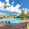 Piscina con lettini, ombrelloni e palme sotto un cielo azzurro.