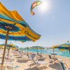 Spiaggia con ombrelloni gialli e blu, mare e aquilone in cielo.