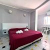 Camera con letto matrimoniale rosso, due applique, tavolino e sedia vicino alla finestra.