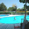 Piscina con deck bianco e persone che nuotano, circondata da alberi e siepi.
