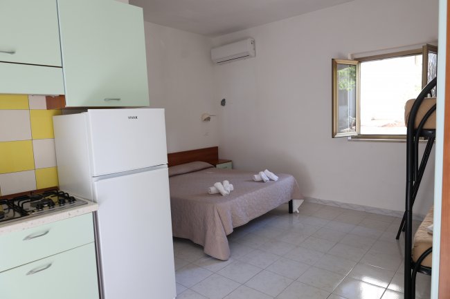 Stanza con letto matrimoniale, letti a castello e cucina.