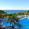 Piscina con vista sul mare e lettini, circondata da palme e vegetazione.