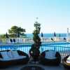 Area piscina con divani, vista mare, lettini e ombrelloni blu.