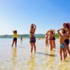 Persone in piedi nell'acqua bassa di una spiaggia, alcune con le mani dietro la testa.