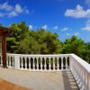Terrazza soleggiata con tavolo bianco e vista panoramica su alberi e mare.