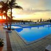 Una piscina con palme e lettini al tramonto, cielo colorato e vista sul mare.