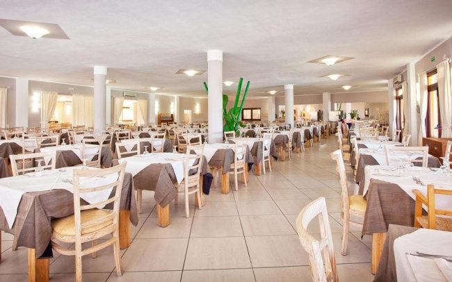 Sala da pranzo ampia con molti tavoli apparecchiati e sedie.